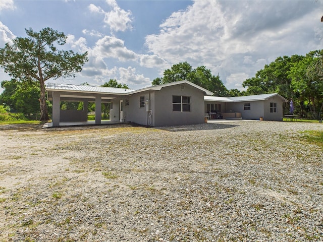 rear view of house with stucco siding, a patio area, and metal roof