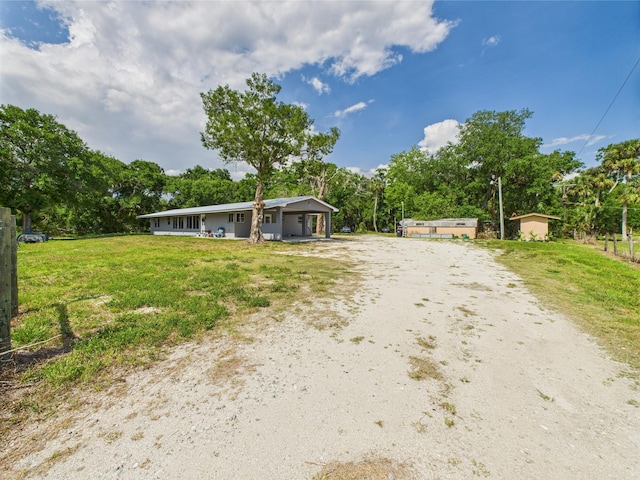 ranch-style house with dirt driveway, view of wooded area, and a porch