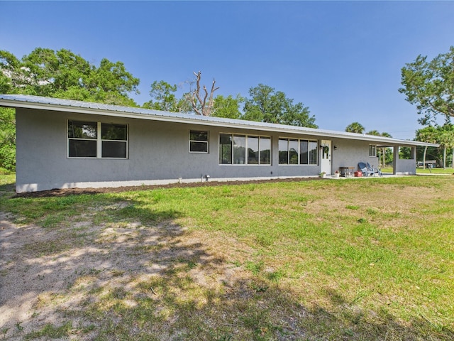 back of property with stucco siding, a lawn, and metal roof