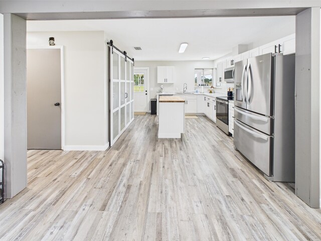 kitchen with appliances with stainless steel finishes, a barn door, light wood finished floors, light countertops, and white cabinets