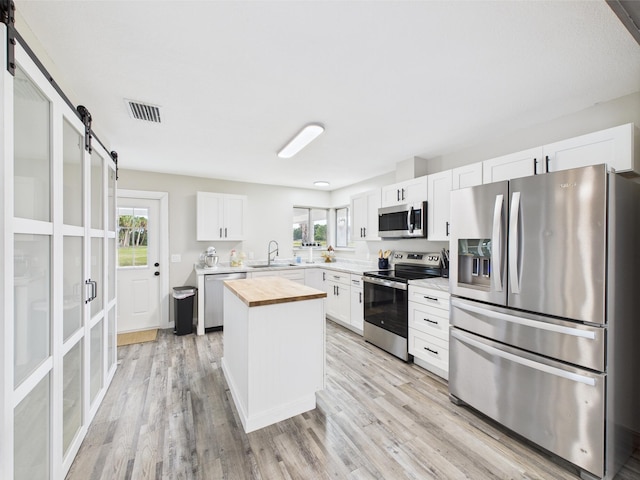 kitchen featuring stainless steel appliances, wooden counters, a barn door, a sink, and plenty of natural light