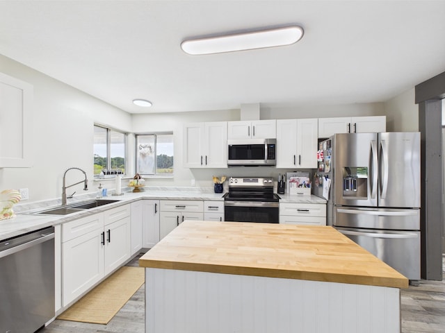 kitchen featuring stainless steel appliances, a sink, wood counters, light wood finished floors, and white cabinets