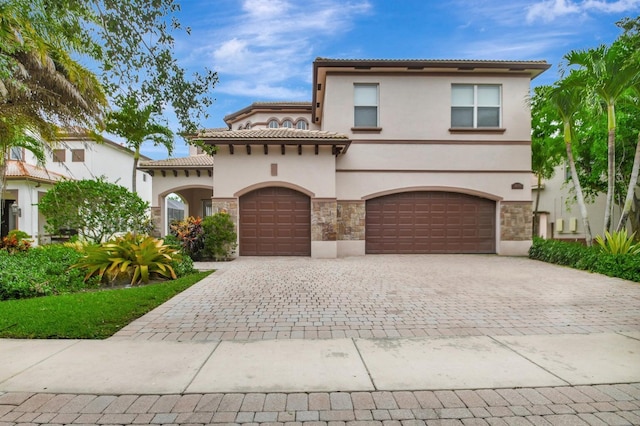 mediterranean / spanish-style home featuring stucco siding, stone siding, decorative driveway, a garage, and a tile roof