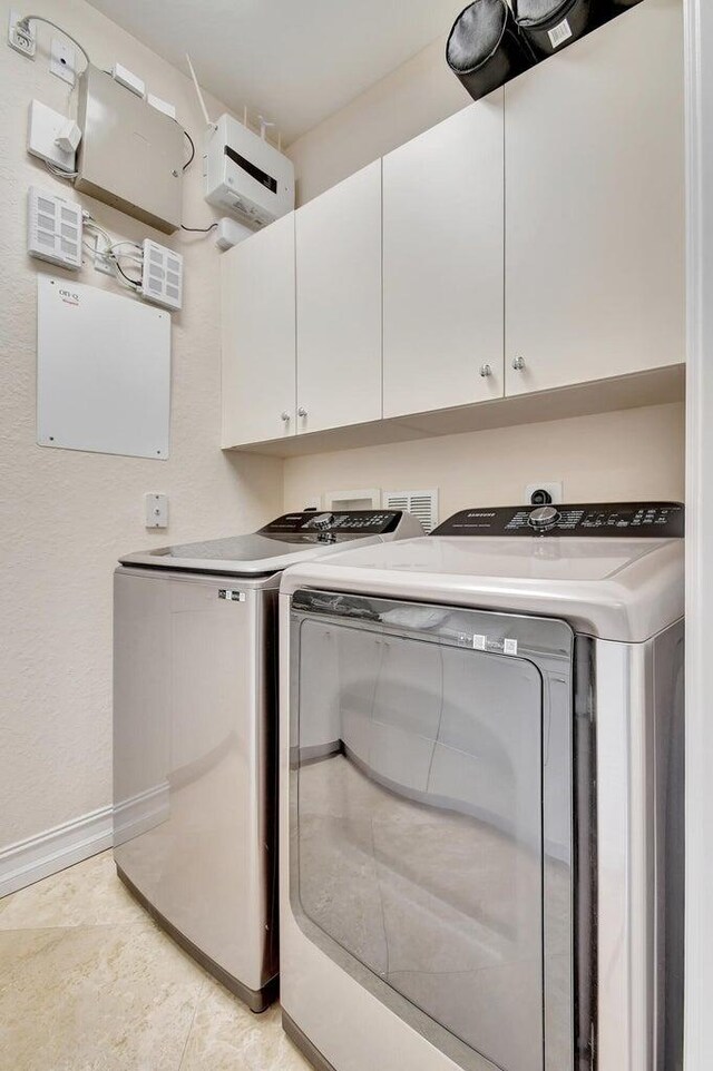 clothes washing area featuring separate washer and dryer, cabinet space, and baseboards