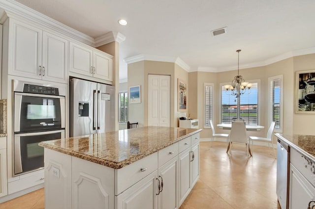 kitchen with appliances with stainless steel finishes, a chandelier, white cabinets, crown molding, and a kitchen island