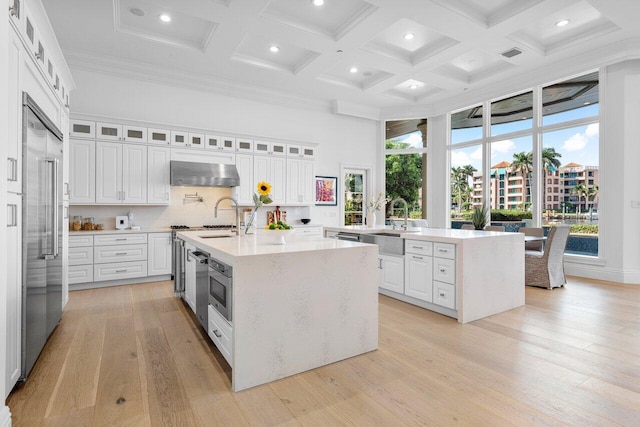 155 SE Spanish Trl, Boca Raton, FL 33432 - kitchen featuring a kitchen island with sink, a high ceiling, wall chimney exhaust hood, coffered ceiling, and a sink