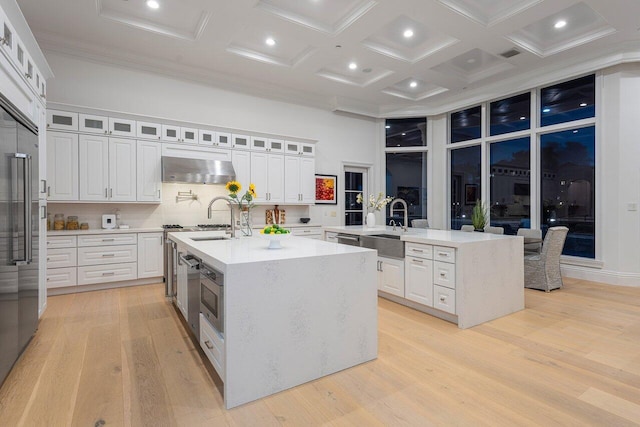 155 SE Spanish Trl, Boca Raton, FL 33432 - kitchen featuring a center island with sink, under cabinet range hood, a high ceiling, coffered ceiling, and light wood finished floors
