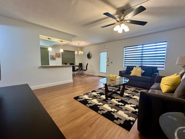 living room with wood finished floors, ceiling fan, baseboards, a chandelier, and a textured ceiling