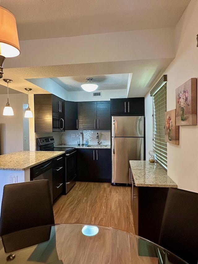 kitchen featuring appliances with stainless steel finishes, a raised ceiling, a sink, dark cabinets, and light wood-type flooring