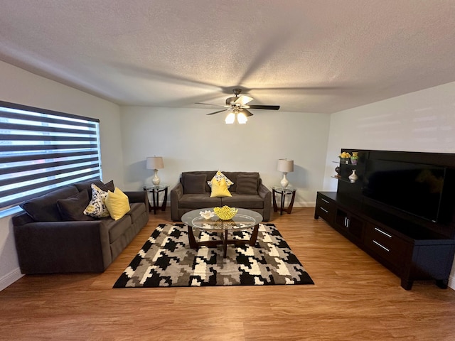 living room featuring a ceiling fan, light wood-style floors, a textured ceiling, and baseboards