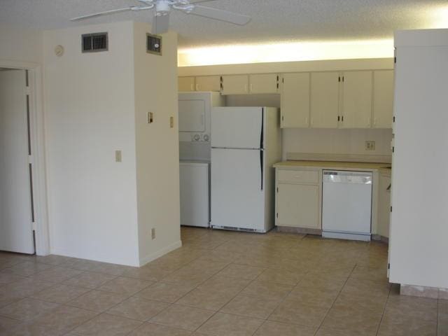 kitchen featuring white appliances, stacked washing machine and dryer, light countertops, a ceiling fan, and cream cabinetry