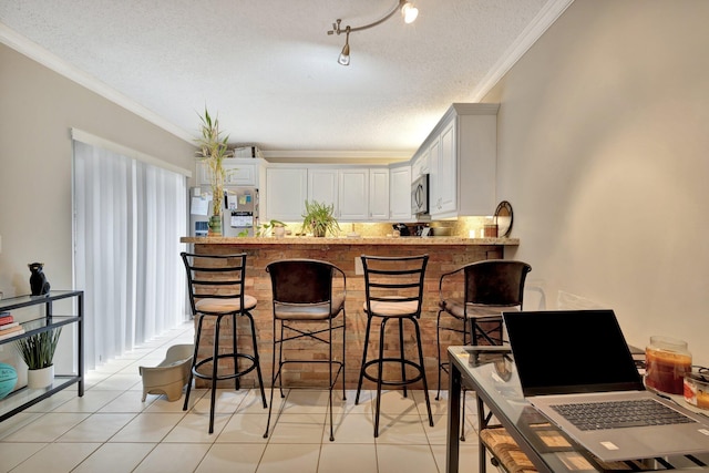 2950 SW 22nd Cir Unit 4C, Delray Beach, FL 33445 - kitchen with stainless steel microwave, ornamental molding, a textured ceiling, light tile patterned floors, and a kitchen bar