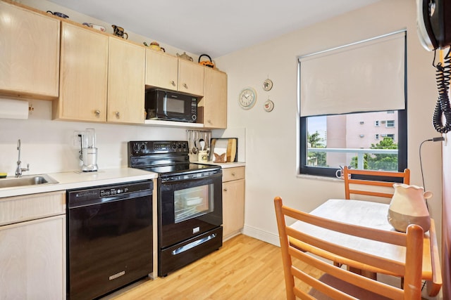 kitchen featuring black appliances, light brown cabinetry, a sink, light countertops, and light wood-type flooring