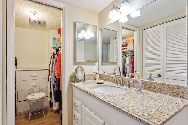 bathroom with a textured ceiling, vanity, wood finished floors, and a spacious closet