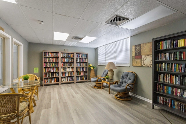 living area featuring wall of books, a drop ceiling, wood finished floors, and baseboards