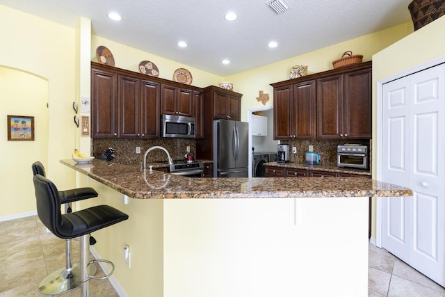 2904 SW Sutton Pl, Palm City, FL 34990 - kitchen with appliances with stainless steel finishes, a peninsula, a breakfast bar, tasteful backsplash, and dark stone counters