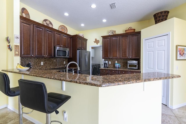 2904 SW Sutton Pl, Palm City, FL 34990 - kitchen featuring stainless steel appliances, a peninsula, washing machine and dryer, a kitchen bar, and backsplash