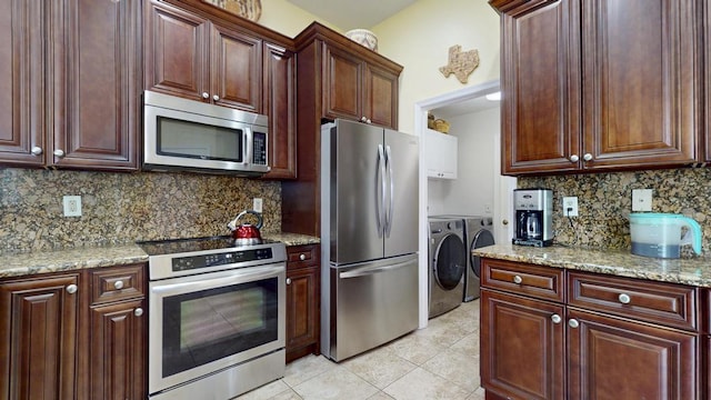 2904 SW Sutton Pl, Palm City, FL 34990 - kitchen featuring appliances with stainless steel finishes, washing machine and dryer, tasteful backsplash, light tile patterned floors, and light stone countertops