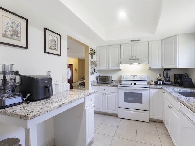 kitchen with white appliances, under cabinet range hood, a tray ceiling, white cabinets, and light tile patterned flooring