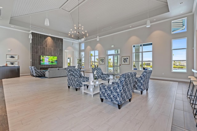 living area featuring a towering ceiling, a raised ceiling, a chandelier, light wood-style flooring, and crown molding