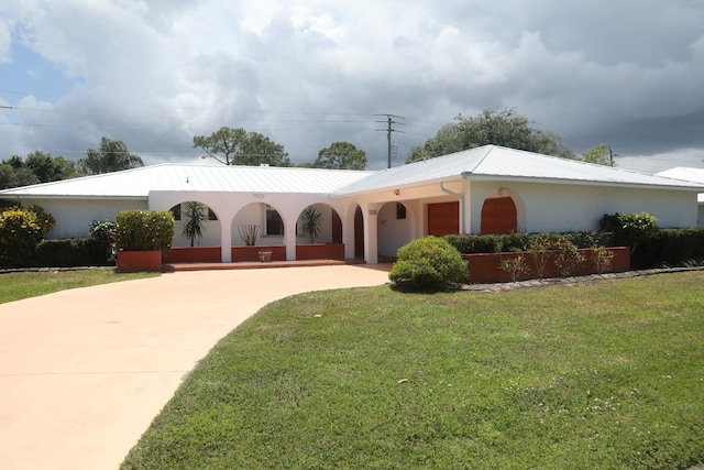 ranch-style house with driveway, a front yard, stucco siding, and metal roof