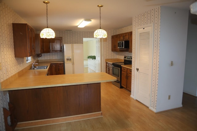 kitchen featuring appliances with stainless steel finishes, wallpapered walls, light countertops, light wood-style flooring, and a sink