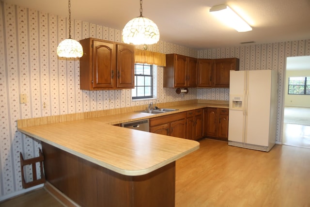kitchen featuring white fridge with ice dispenser, wallpapered walls, a sink, light countertops, and a peninsula