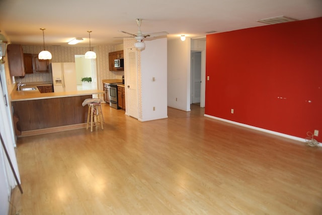 kitchen with stainless steel appliances, wallpapered walls, a sink, a peninsula, and light wood-style flooring