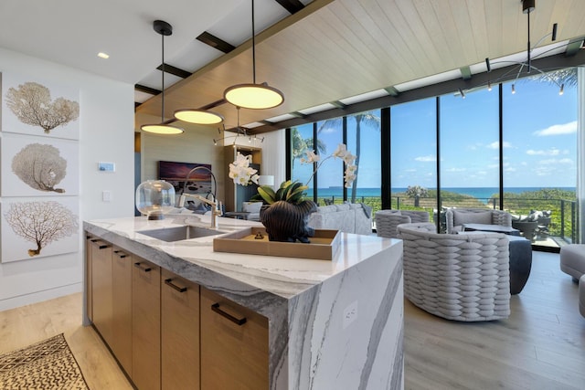 kitchen with floor to ceiling windows, light stone counters, light wood finished floors, a sink, and hanging light fixtures