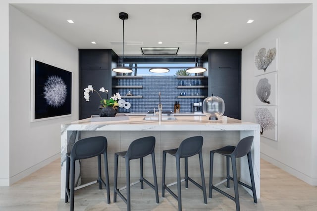 bar area with a sink, hanging light fixtures, light wood finished floors, and recessed lighting