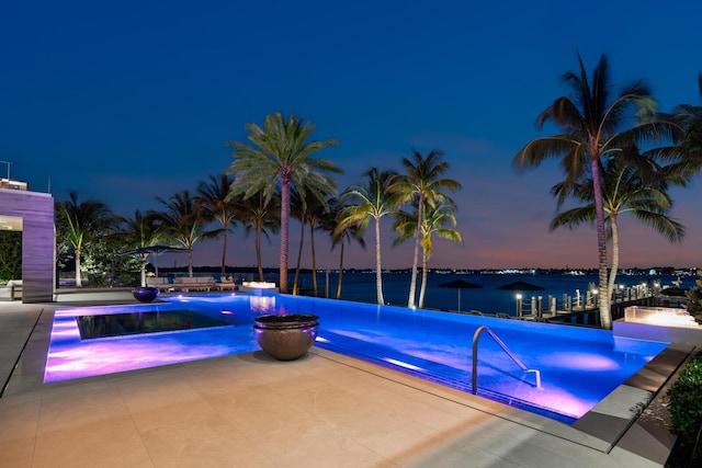 pool at dusk with an infinity pool, a patio, and a water view