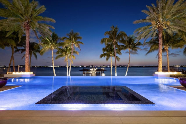 pool at dusk with a water view and a pool with connected hot tub