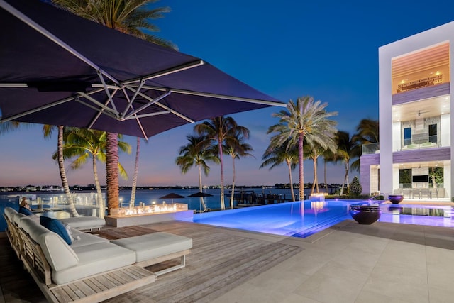 pool at dusk featuring an infinity pool, a water view, and a patio area