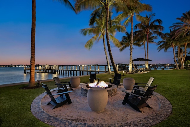 patio terrace at dusk featuring an outdoor fire pit, a yard, and a water view
