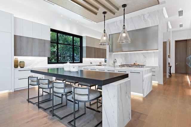 kitchen featuring modern cabinets, a center island with sink, backsplash, light countertops, and light wood-style flooring