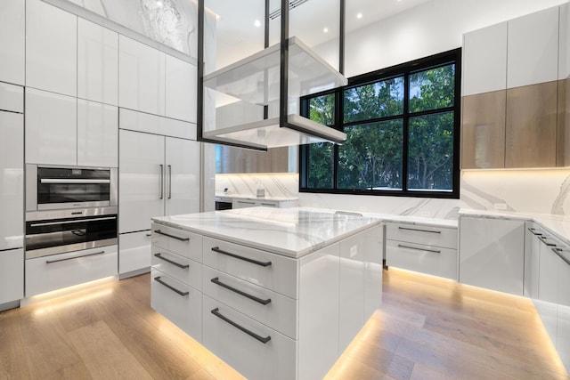 kitchen featuring modern cabinets, oven, light wood-style flooring, light stone countertops, and a warming drawer