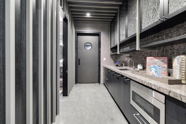 kitchen with stainless steel microwave, a sink, light stone countertops, and open shelves
