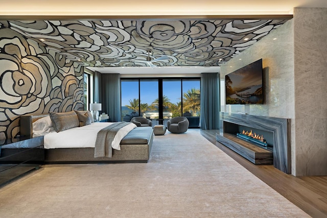 bedroom with a glass covered fireplace and wood finished floors