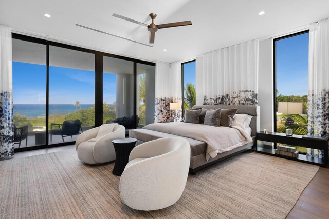bedroom featuring a wall of windows, wood finished floors, multiple windows, a ceiling fan, and a water view