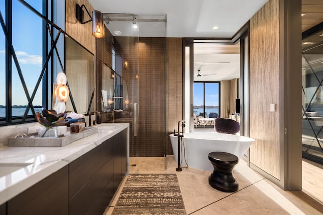 bathroom featuring vanity, a freestanding tub, a ceiling fan, floor to ceiling windows, and a water view