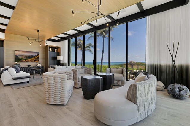 living room featuring a chandelier, a wall of windows, a water view, wood finished floors, and a high ceiling