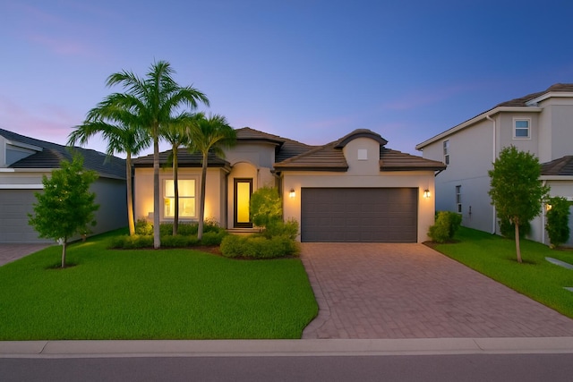view of front facade featuring decorative driveway, an attached garage, a lawn, stucco siding, and a tile roof