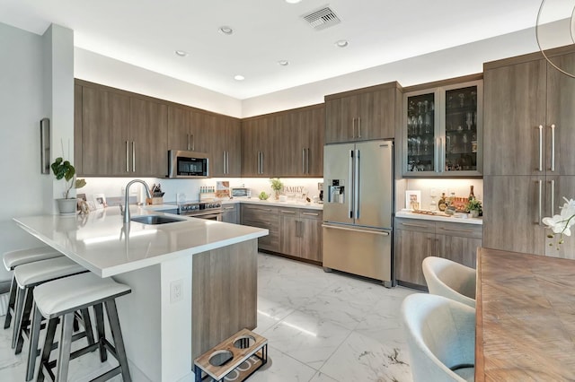 kitchen with stainless steel appliances, light marble finish flooring, a breakfast bar area, a sink, and glass insert cabinets