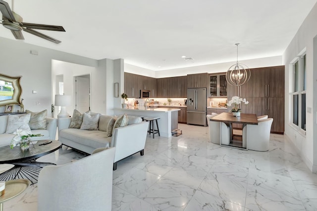 living area featuring a chandelier, light marble finish flooring, and ceiling fan