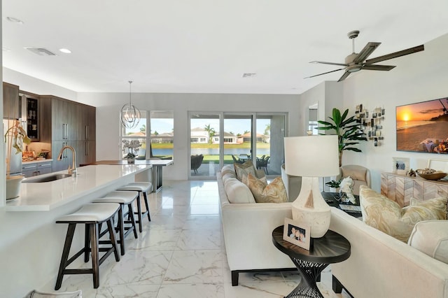 living room featuring light marble finish flooring, a ceiling fan, a water view, and recessed lighting