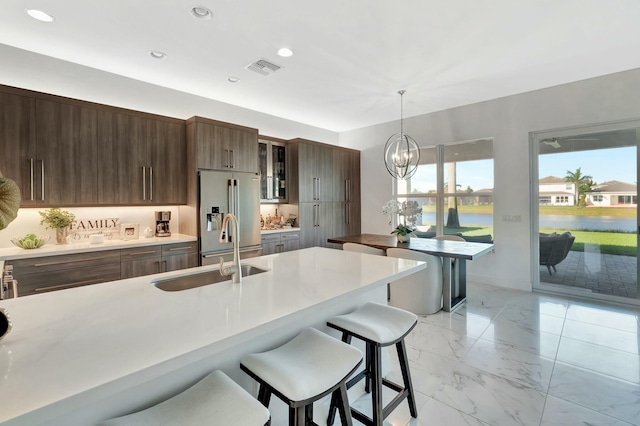 kitchen featuring high end fridge, a sink, light marble finish flooring, a kitchen bar, and light countertops