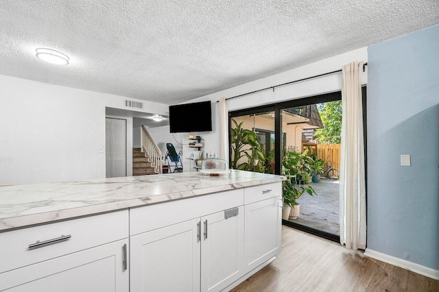 4059 Palm Bay Cir Unit C, West Palm Beach, FL 33406 - kitchen featuring light wood-style flooring, a textured ceiling, light stone countertops, white cabinets, and baseboards
