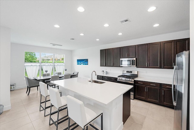 kitchen featuring stainless steel appliances, a sink, recessed lighting, a kitchen breakfast bar, and a center island with sink