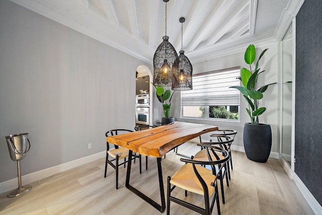 dining space with light wood-type flooring, arched walkways, baseboards, and beam ceiling