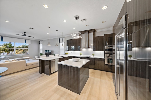 kitchen featuring modern cabinets, wall chimney exhaust hood, appliances with stainless steel finishes, open floor plan, and a sink